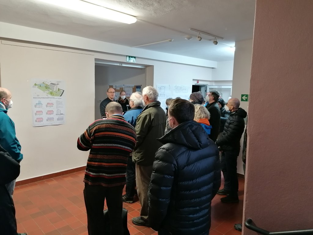 Eine Besuchergruppe hört in einem Flur einem Vortrag vor verschiedenen Infoplakaten zu.
