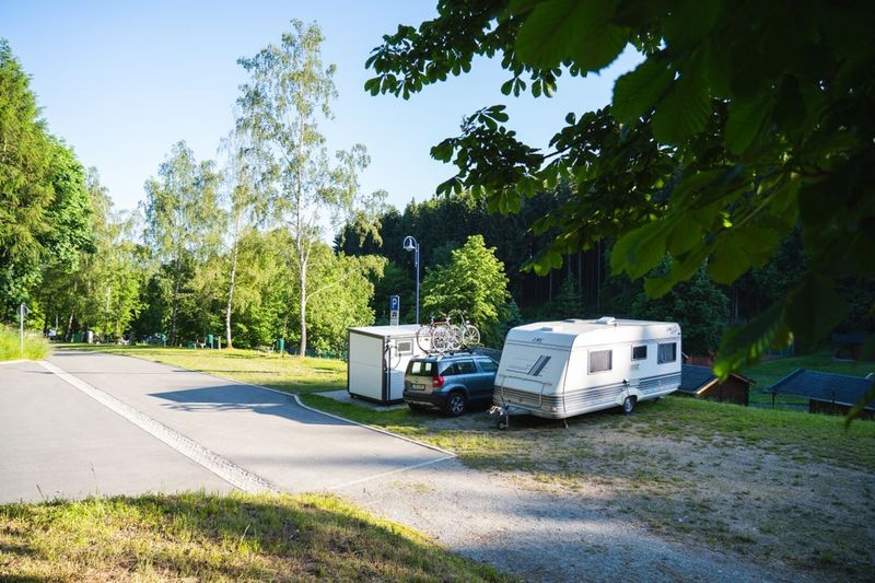 Idyllischer Campingplatz im Grünen mit einem Wohnwagen-Gespann, Fahrrädern und einer weiten Waldkulisse. (Link öffnet das Foto vergrößert in einem Popupfenster)