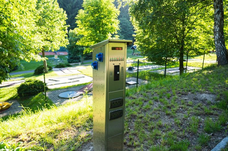 Query successful Eine Edelstahlsäule für Strom- oder Münzeinwurf im Vordergrund einer Minigolfanlage im Grünen. (Link öffnet das Foto vergrößert in einem Popupfenster)