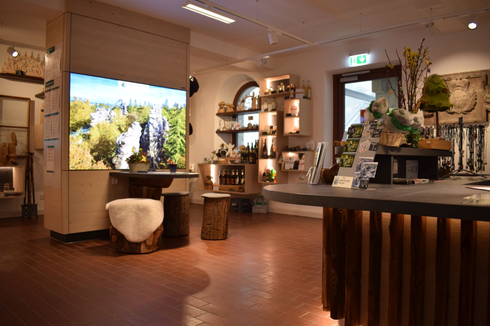 Tourist-Info mit großem Monitor, rustikalen Hockern und Souvenir-Regalen (Link öffnet Bild vergrößert in einem Popupfenster)