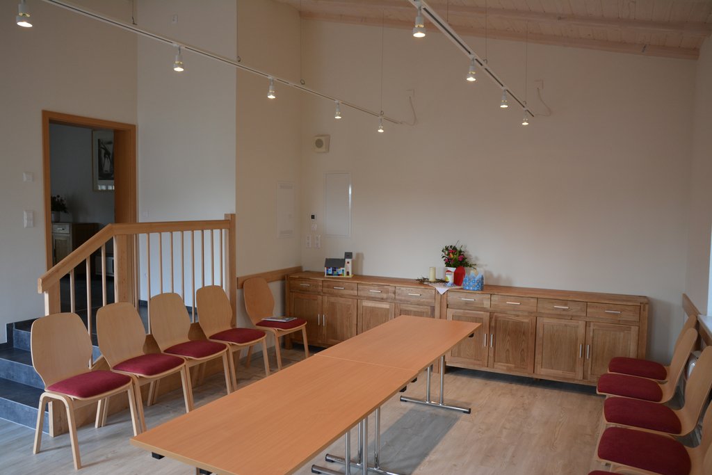 Heller Gemeinschaftsraum mit Tischen, Stühlen und Holzkommode (Link öffnet Bild vergrößert in einem Popupfenster)