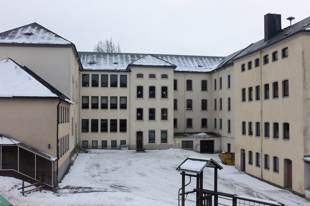 Verschneiter Schulinnenhof in Geyer mit mehrstöckigen Gebäudeteilen und Spielgerät