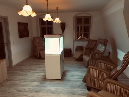 Gemütlicher Ruheraum mit beleuchtetem Aquarium, mehreren Sesseln und warmem Deckenlicht.