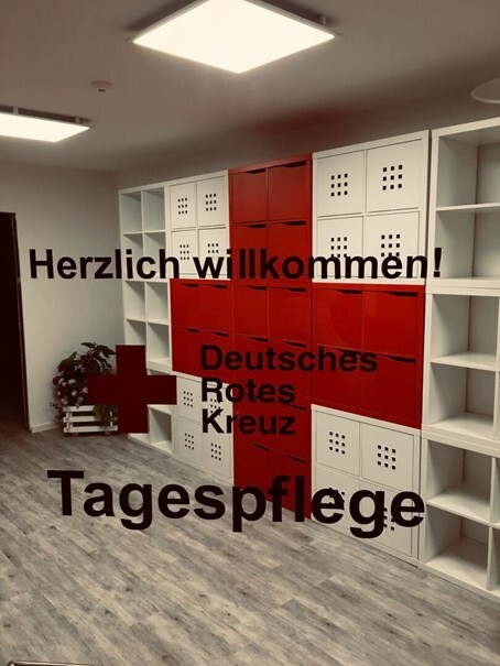 Eingangsbereich der DRK-Tagespflege mit weiß-rotem Regalsystem und Begrüßungsschriftzug auf Glas.