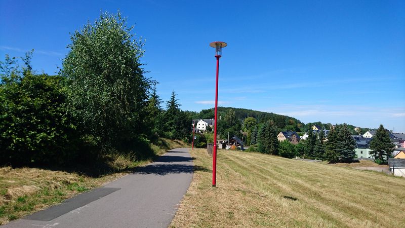 Asphaltierter Weg mit roter Laterne am Hang mit Blick auf eine Siedlung